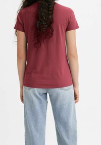 Maroon t-shirt med mjuk textur, korta ärmar och åtsittande design, matchad med ljusblå, löst sittande, högmidjade jeans.