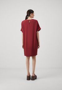 Röd knälång klänning med korta ärmar, texturerad tyg och ett nyckelhålöppning på baksidan. Bärs med bruna plattformsskor.
