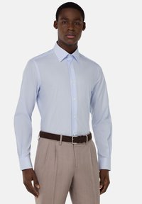 Camicia button-up a righe blu chiaro con colletto, maniche lunghe e design aderente, abbinata a pantaloni beige chiaro plissettati e una cintura scura.