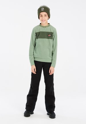Sweatshirt en polaire verte avec des rayures noires et un logo, associé à un pantalon noir et un bonnet vert. Texture lisse, coupe décontractée.