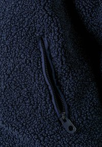 Marineblauwe fleece stof met een gestructureerd, pluizig oppervlak. Voorzien van een zwarte ritsopening langs de naad voor functionaliteit.