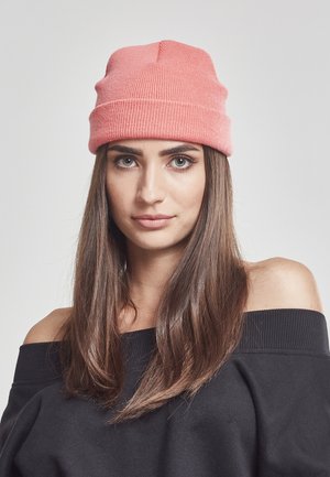 Rosa strikket lue med ribbestruktur, med en midtseam, båret med en svart av-shoulder sweatshirt. Lange, rette brune hår er synlige.
