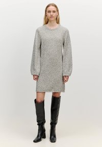 Gestricktes graues Kleid mit strukturierter Silhouette, langen Puffärmel und strukturierter Oberfläche, kombiniert mit knielangen schwarzen Lederstiefeln.