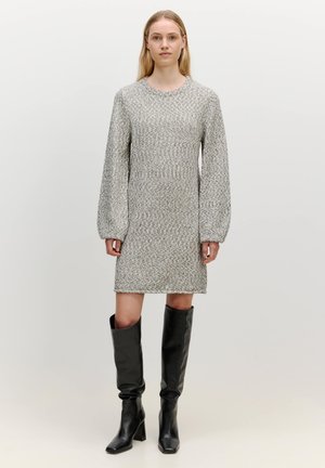 Gestricktes graues Kleid mit strukturierter Silhouette, langen Puffärmel und strukturierter Oberfläche, kombiniert mit knielangen schwarzen Lederstiefeln.