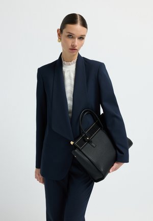 Traje a rayas navy con una silueta estructurada, combinado con un bolso de cuero negro con detalles dorados y una textura suave.