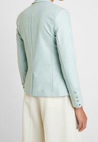 Skräddarsydd mintgrön jacka med en strukturerad design, som har en slagkrage och knäppta manschetter, tillverkad av ett mjukt och lätt tyg.