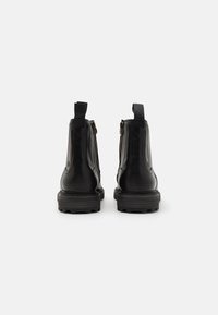 Botas de cuero negras hasta el tobillo con un diseño elegante, que cuentan con un zipper lateral y una tira de agarre, suela de goma texturada y acabado de superficie suave.