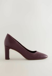 Pumps dengan hak tinggi berwarna burgundy, terbuat dari kulit, dengan ujung bulat dan finishing tekstur. Memiliki hak yang chunky dan desain minimalis.