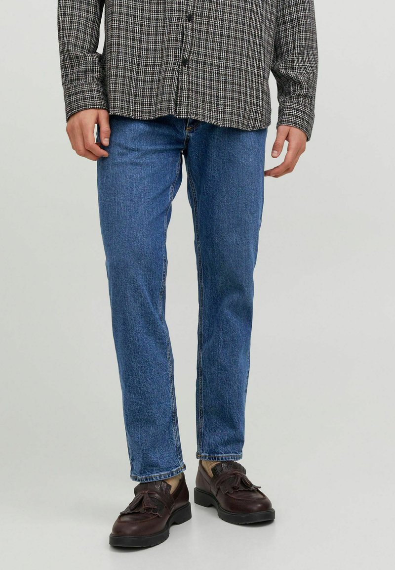 Camisa a cuadros en blanco y negro combinada con jeans rectos azules y zapatos marrón oscuro con detalles de borlas.