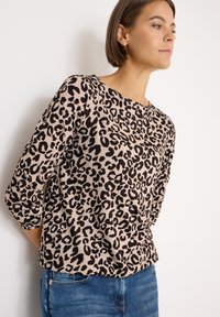 Top lungo a maniche con stampa leopardata in beige con accenti neri, scollo rotondo e vestibilità morbida, abbinato a jeans blu denim. Tessuto dalla texture morbida.
