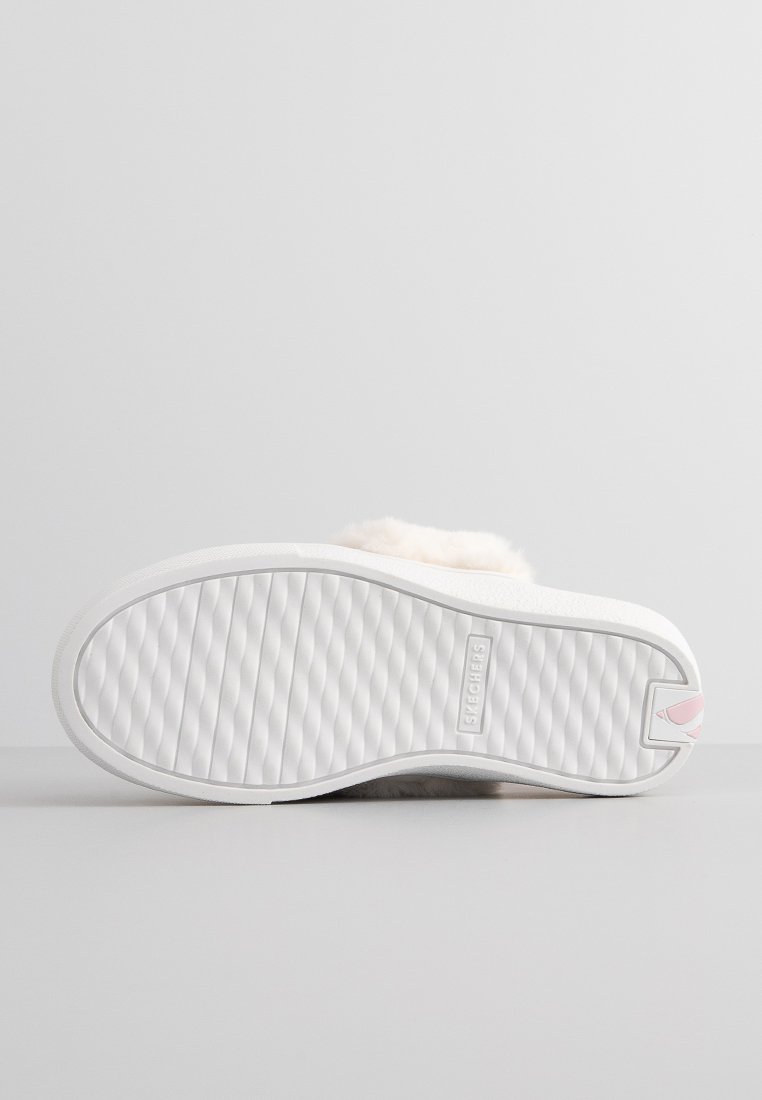 Zapatilla blanca sin cordones con parte superior de felpa, textura suave y suela de goma texturizada que presenta un sutil patrón en zigzag.