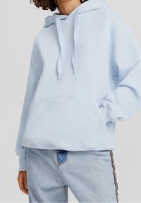 Sudadera azul claro hecha de tela suave, con un bolsillo canguro, capucha con cordón y puños acanalados. Combinada con jeans azul claro.