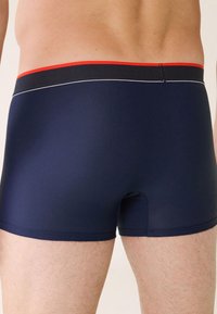 Maillots de bain bleu marine avec une finition texturée. Dotés d'une ceinture élastique rouge et blanche. Longueur mi-cuisse avec un design ajusté.