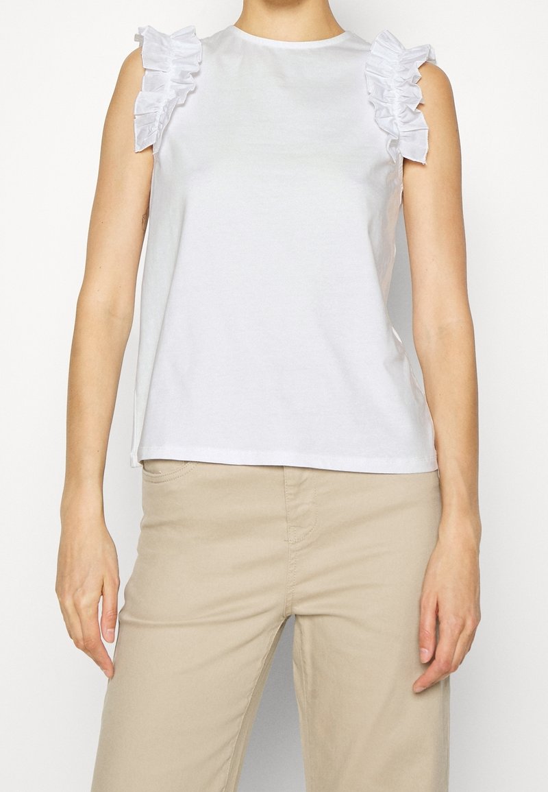 Biała top bez rękawów z falbaniastymi akcentami na ramionach, wykonany z gładkiego materiału. Prosty krój, zestawiony z beżowymi spodniami.