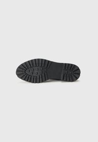 Suela de zapato de goma con un dibujo en relieve, que presenta surcos profundos y bordes redondeados. Color predominantemente negro, diseño robusto para proporcionar tracción.