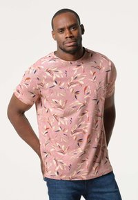 Korte mouwen, ronde hals t-shirt van zacht roze stof met een bloemenpatroon met bladeren in gedempte kleuren. Gedorven met blauwe spijkerbroeken.
