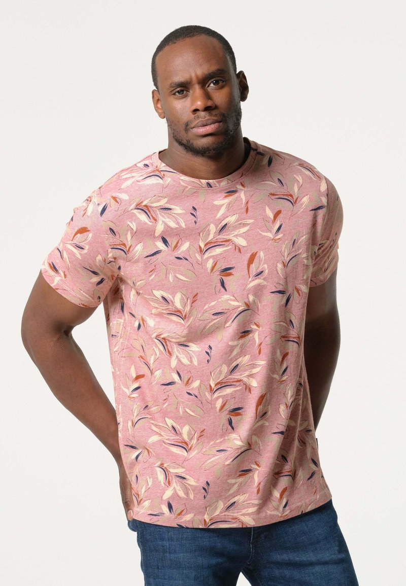 Korte mouwen, ronde hals t-shirt van zacht roze stof met een bloemenpatroon met bladeren in gedempte kleuren. Gedorven met blauwe spijkerbroeken.