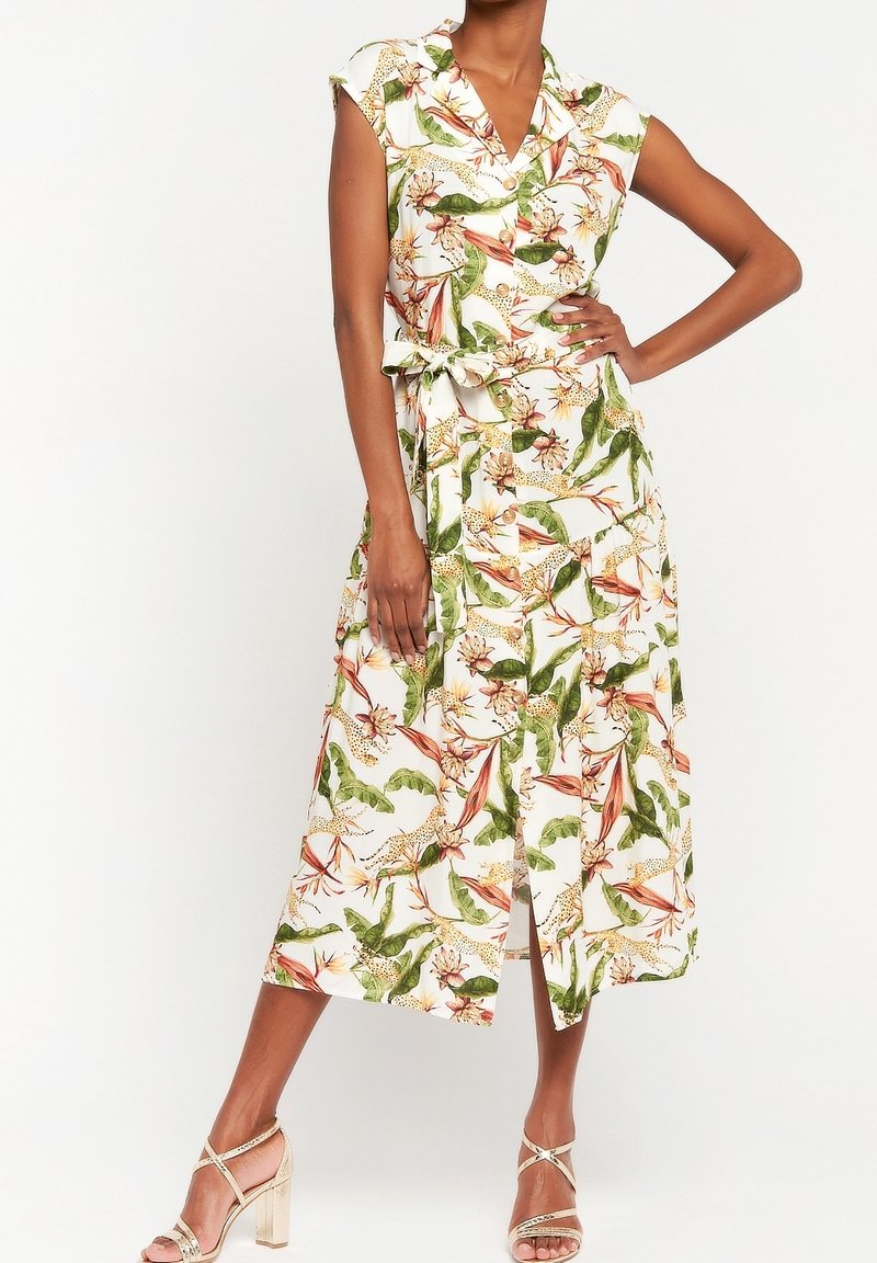 Kremowa sukienka w kwiaty z zielonymi liśćmi i pomarańczowymi kwiatami, o długości średniej, z wiązanym paskiem w talii i rękawami typu cap, wykonana z lekkiego materiału.