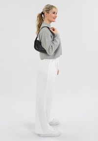 Grijs gebreid crop sweater gecombineerd met witte wijde broek en witte sneakers. Een kleine zwarte tas wordt aan de schouder gedragen.