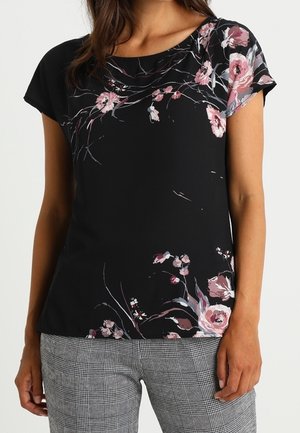 Top corto nero a maniche corte con motivo floreale in rosa e bianco, dotato di scollo rotondo e tessuto morbido. Abbinato a pantaloni grigi con fantasia.
