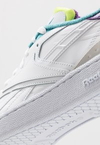 Vita sneakers med texturerad gummisula, med turkosa och lila accenter, detaljerad sömnad och en vadderad tunga i klart neongul.