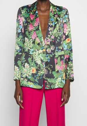 Tailored floral blazer with green, pink, and blue flowers over black, paired with bright magenta pants, worn by person with dark skin tone.