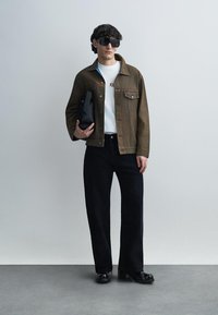 Καφέ τζιν μπουφάν με τσέπες, λευκό t-shirt, μαύρο τζιν με φαρδιά μπατζάκια και παπούτσια με πάτο πλατφόρμας. Μαύρα γυαλιά ηλίου και κρατάει μια μαύρη τσάντα.