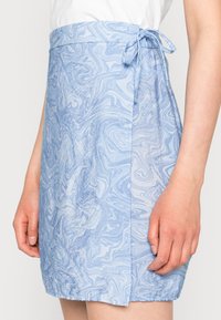 Vaaleansininen marmorikuvioinen kietaisuhame, jossa on sivusolmu, päällä henkilö yksinkertaisella taustalla.