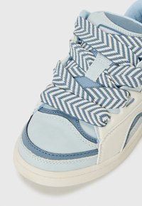 Low-top sneaker featuring a smooth blue and cream leather upper, blue herringbone patterned laces, and a textured rubber sole.