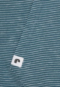 Katoenen stof in teal en witte strepen, met een klein label met een zwart logo. Zachte textuur met een gelijkmatige breipatroon.