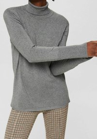 Grijze coltrui van een zachte gebreide stof met lange mouwen en geribbelde manchetten, gecombineerd met een geruite broek.