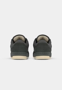 Black leather sneakers with a low-cut design, smooth texture, and beige rubber soles. Features include subtle perforations and stitching details.