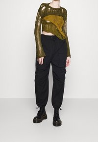 Strikket cropped sweater i olivengrøn med udskæringer, parret med sorte cargo bukser med lommer og snor. Sorte kampstøvler.