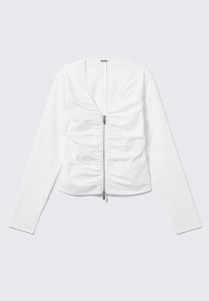 Wit langarmshirt met V-hals, rits aan de voorkant en geplooide stofdetails op het lichaam, plat gelegd op een lichte achtergrond.