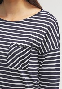 Námořnický a bílý pruhovaný top s dlouhým rukávem a kulatým výstřihem, který má kapsu na levé straně hrudi a malou nášivku "ONLY" na kapse.