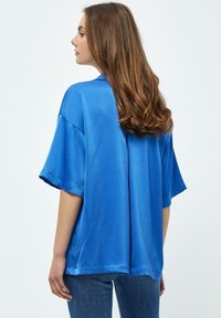 Camisa de corte holgado de manga corta en color azul, confeccionada en una tela suave. Presenta un diseño sencillo, con dobladillo recto y ajuste relajado.