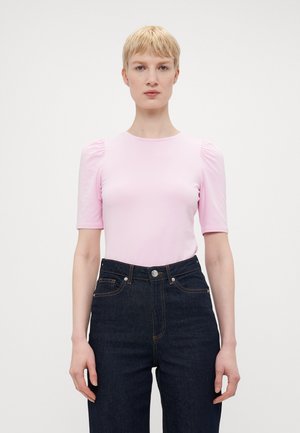 Světle růžový krátký rukáv top s vypouklými rameny, vyrobený z elastické tkaniny. Spárovaný s tmavě modrými džíny s vysokým pasem.