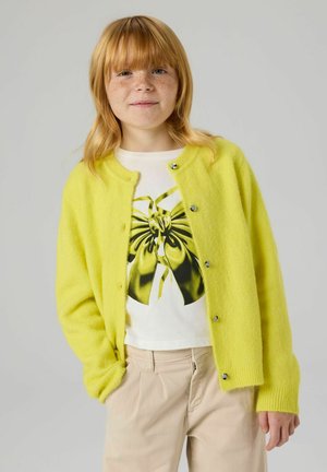 Lime green, fuzzy knit cardigan with round neckline and buttons, paired with a white t-shirt featuring a black and green graphic design.