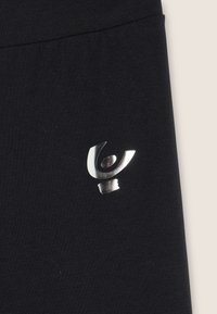 Tessuto nero con una texture liscia presenta un logo argento ben visibile sul lato sinistro, che mostra una figura stilizzata in movimento.