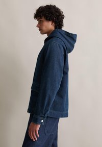 Dunkelblaue Denimjacke mit Kapuze, ausgestattet mit einer Fronttasche, langen Ärmeln und knöpfbaren Manschetten. Glatte Textur und lässiges Design.