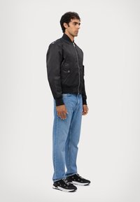Svart bomberjacka med dragkedja, sidofickor, ribbstickade muddar; tillsammans med ljusblå raka jeans och svarta sneakers med vita detaljer.