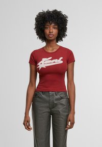 Rode, aansluitende t-shirt met korte mouwen met een wit grafisch logo. Gecombineerd met donkergrijze, iets losse jeans met zakken.