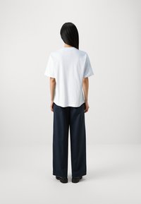 T-shirt blanc à manches courtes et coupe décontractée associé à un pantalon large bleu marine. Le tissu semble lisse avec des coutures minimales et un design simple.