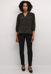 Blouse florale sombre avec un décolleté en V, un col froncé et des manches trois-quarts, associée à un pantalon noir ajusté et des talons noirs.