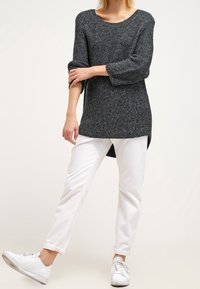 Grå stickad tröja med vid halsringning och 3/4-långa ärmar, kombinerad med vita raka jeans och vita sneakers.