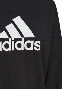 Sudadera negra con un gran logo blanco de "Adidas" y tres rayas diagonales, con una textura suave y un corte relajado.