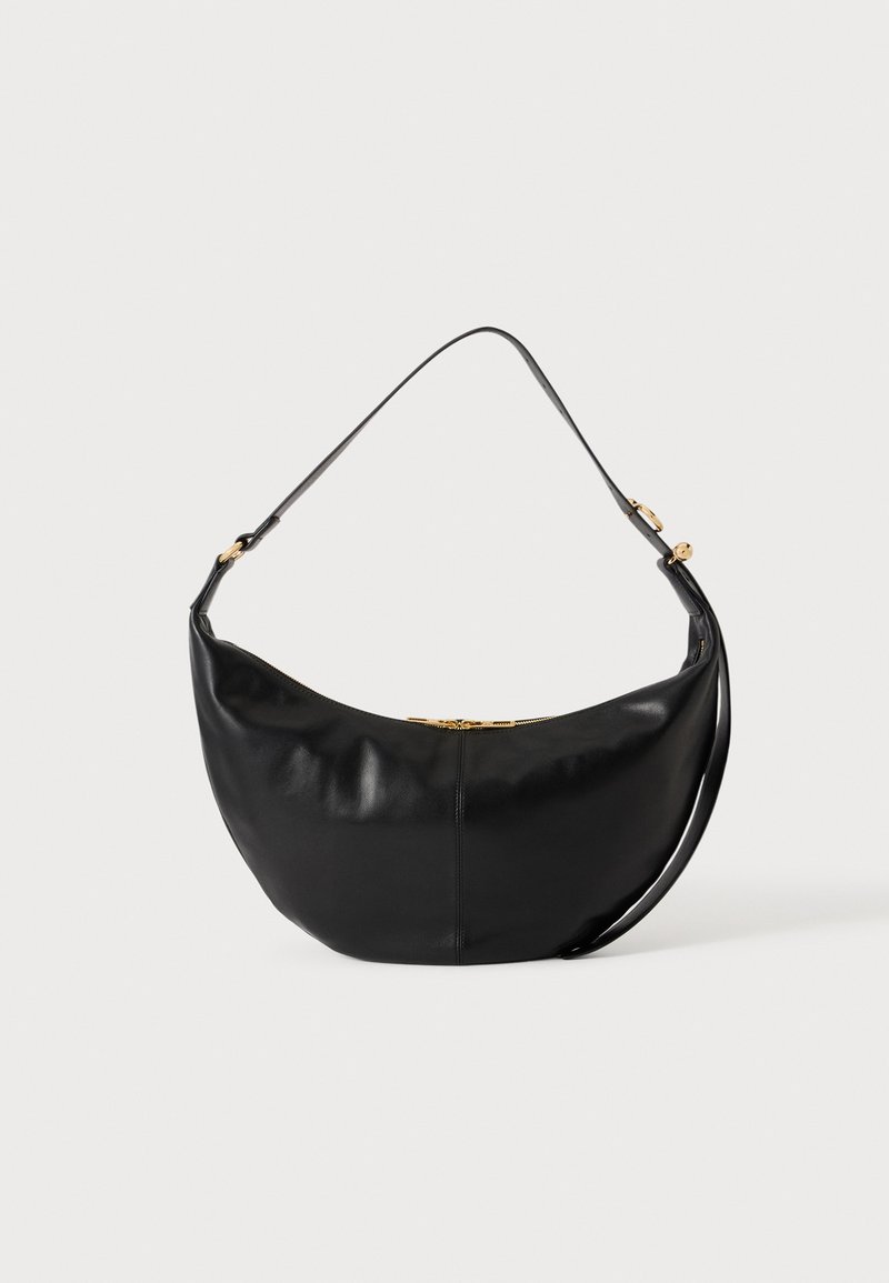 Sac à main en cuir noir en forme de croissant avec une bandoulière simple et un détail de fermeture éclair dorée sur fond uni.