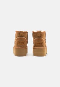 Bottines en daim marron avec une doublure moelleuse, dotées d'une semelle en caoutchouc texturée et d'une couture en zigzag contrastante le long des bords.