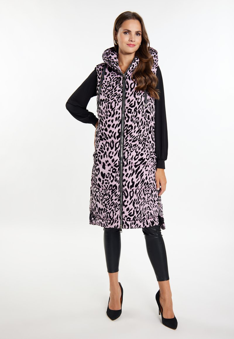 Langer, ärmelloser pinker Vest mit schwarzem Leopardenmuster, ausgestattet mit einem hohen Kragen und einem Reißverschluss vorne. Kombiniert mit schwarzen Leggings und spitzen Absätzen.