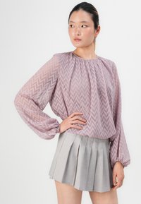 Long-sleeve, light purple blouse with a zigzag pattern, paired with a gray pleated skirt. The blouse features gathered cuffs and neckline.